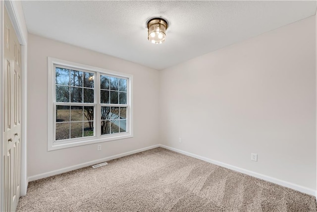 unfurnished room with a textured ceiling, carpet flooring, visible vents, and baseboards