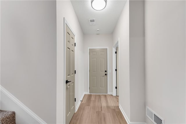 corridor with light wood-type flooring, visible vents, and baseboards