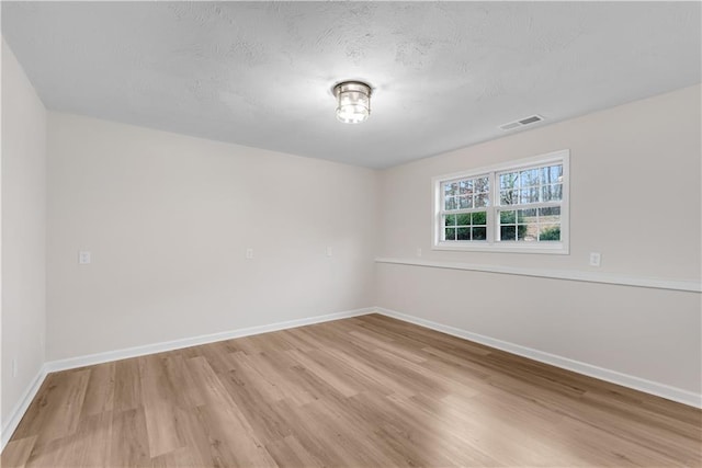 unfurnished room with light wood-type flooring, visible vents, and baseboards