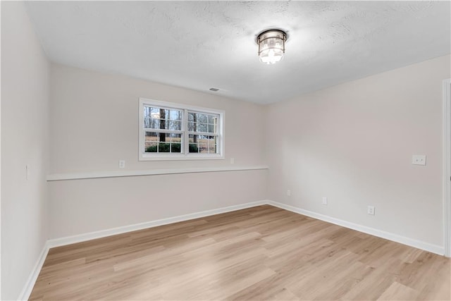 unfurnished room with baseboards, a textured ceiling, visible vents, and light wood-style floors