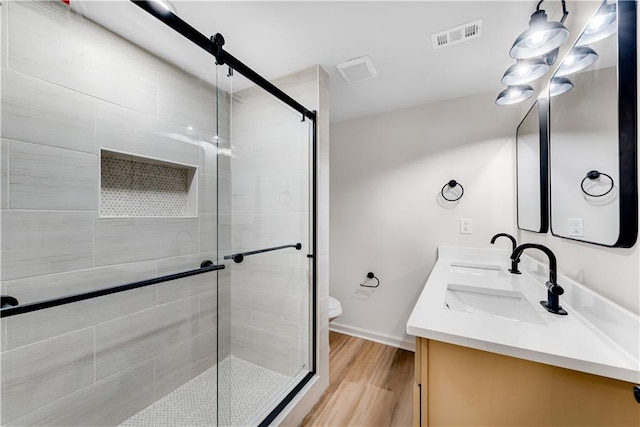 full bathroom with double vanity, visible vents, wood finished floors, a shower stall, and a sink