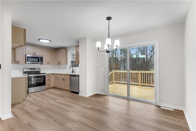 kitchen with decorative backsplash, appliances with stainless steel finishes, hanging light fixtures, light countertops, and light brown cabinetry