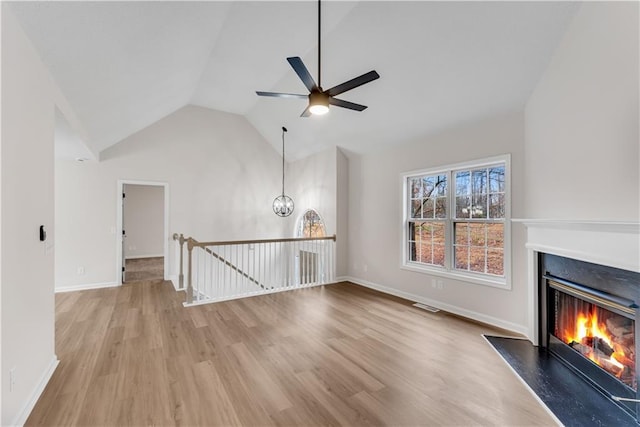 unfurnished living room featuring visible vents, vaulted ceiling, wood finished floors, and a glass covered fireplace