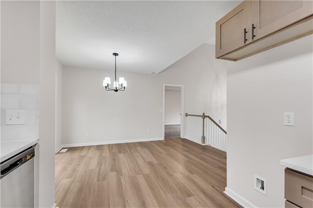 unfurnished dining area featuring baseboards, a textured ceiling, light wood-style flooring, and a notable chandelier