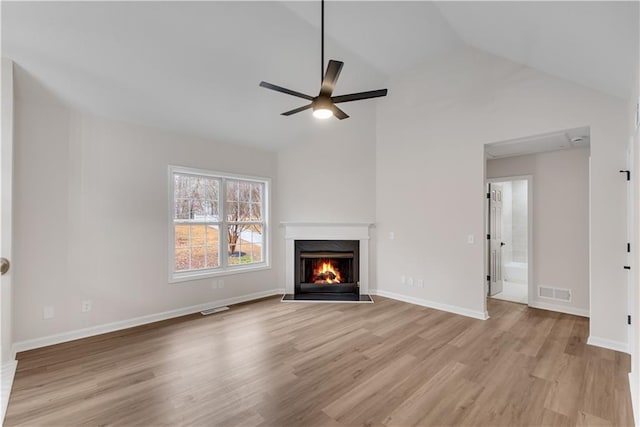 unfurnished living room with a warm lit fireplace, light wood-style flooring, visible vents, baseboards, and vaulted ceiling