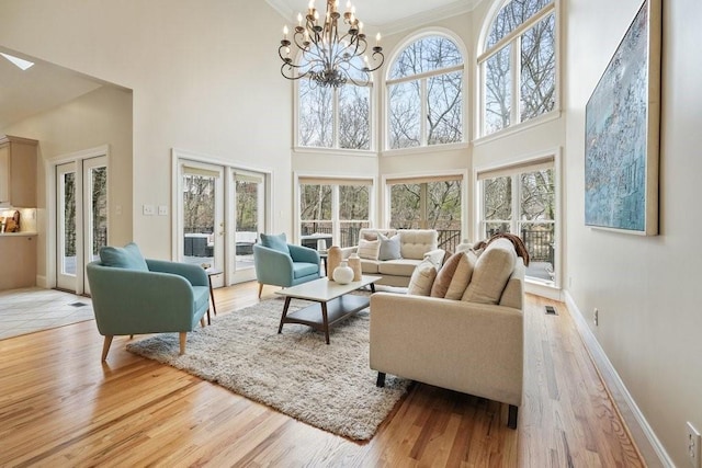 living area with baseboards, french doors, an inviting chandelier, and light wood-style floors