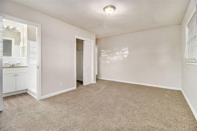 unfurnished bedroom featuring carpet flooring, ensuite bathroom, a closet, and sink