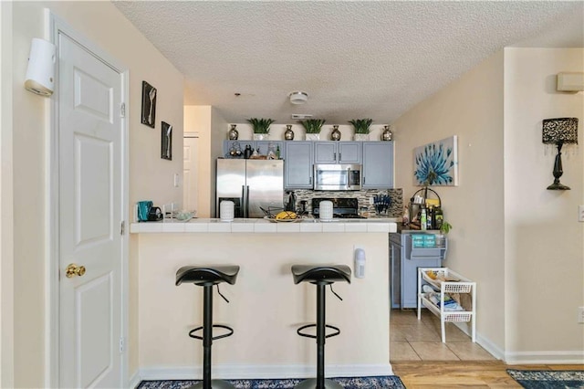 kitchen featuring kitchen peninsula, appliances with stainless steel finishes, a breakfast bar, gray cabinets, and tile counters