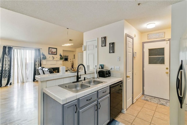 kitchen with black dishwasher, sink, a textured ceiling, tile counters, and gray cabinets