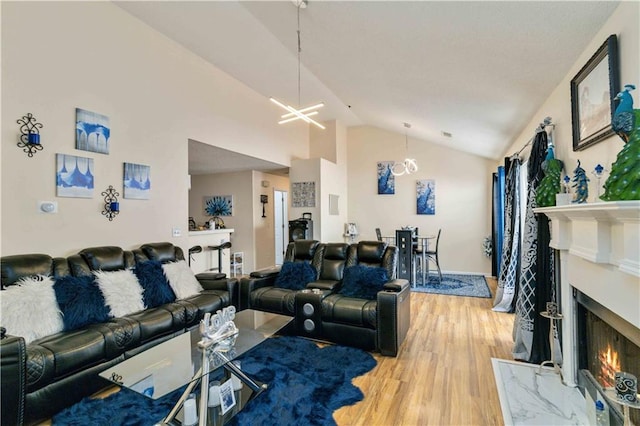 living room with high vaulted ceiling, wood-type flooring, a chandelier, and a high end fireplace