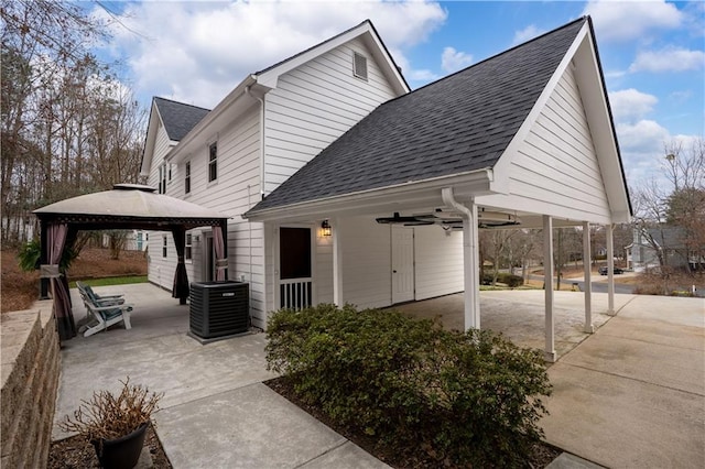 view of property exterior with roof with shingles, central air condition unit, a gazebo, a patio area, and ceiling fan