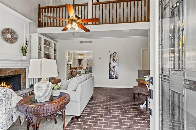 living room featuring brick floor, a fireplace, visible vents, ceiling fan, and baseboards