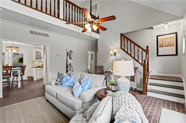 living room with a high ceiling, brick floor, stairs, and visible vents