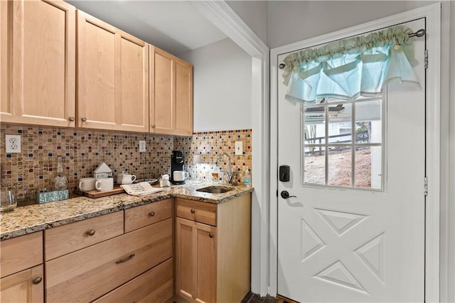 kitchen featuring light stone countertops, a sink, backsplash, and light brown cabinetry