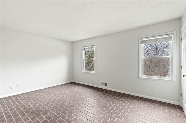 spare room featuring brick floor, visible vents, and baseboards