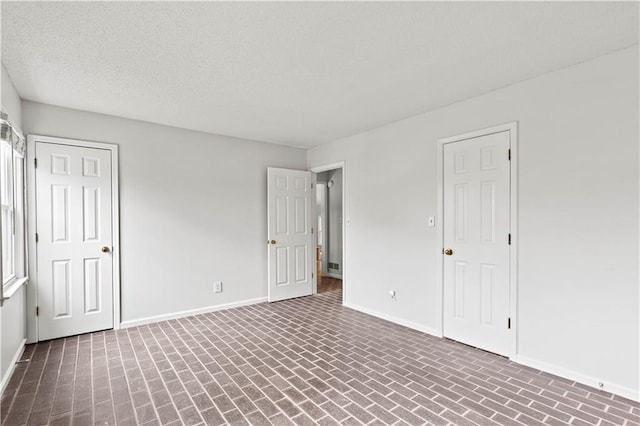 unfurnished bedroom with brick floor, a textured ceiling, and baseboards