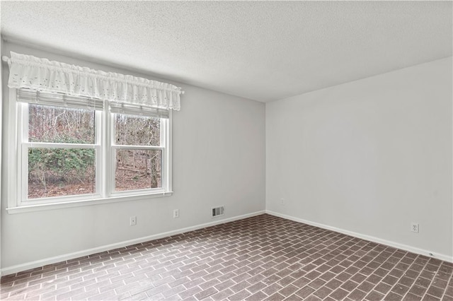 unfurnished room featuring a textured ceiling, brick floor, visible vents, and baseboards