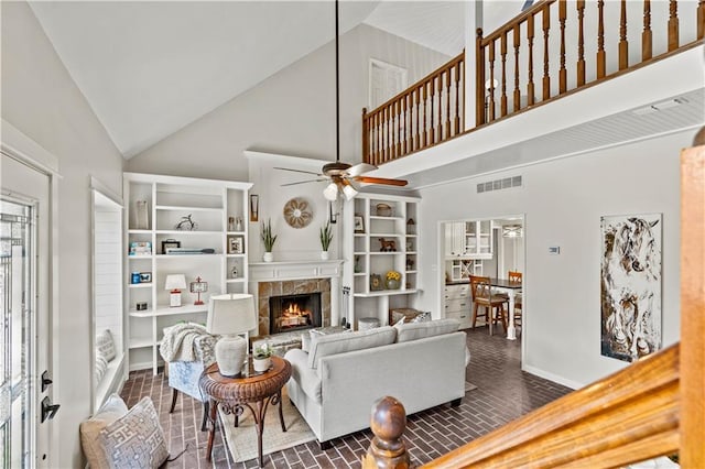 living area with high vaulted ceiling, brick floor, visible vents, a ceiling fan, and a lit fireplace