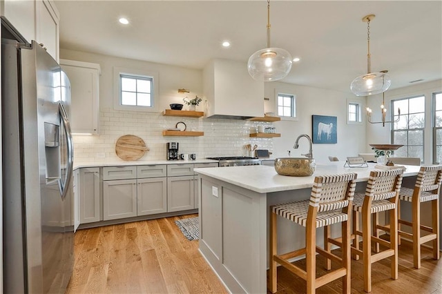 kitchen featuring decorative backsplash, stainless steel fridge, a kitchen island with sink, and hanging light fixtures