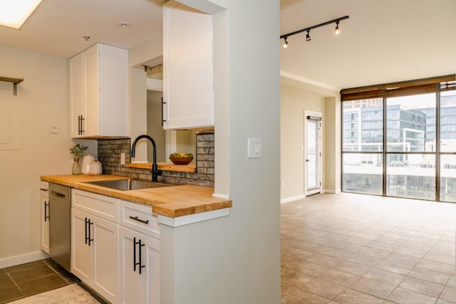 kitchen with tasteful backsplash, baseboards, butcher block counters, white cabinetry, and a sink