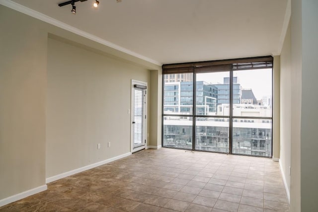 spare room featuring rail lighting, baseboards, floor to ceiling windows, and ornamental molding