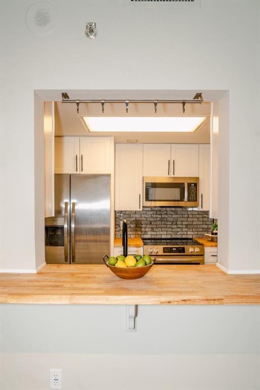 kitchen featuring stainless steel appliances, white cabinets, wooden counters, and backsplash