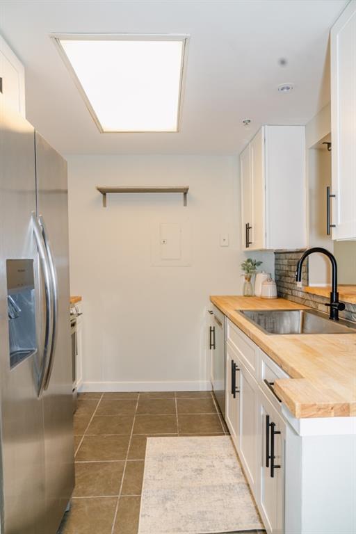 kitchen featuring white cabinets, butcher block countertops, tile patterned flooring, stainless steel appliances, and a sink