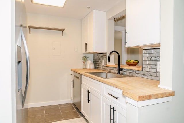 kitchen with butcher block counters, white cabinetry, backsplash, and a sink