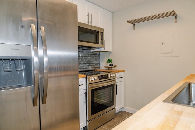 kitchen with stainless steel appliances, butcher block countertops, white cabinetry, decorative backsplash, and tile patterned floors