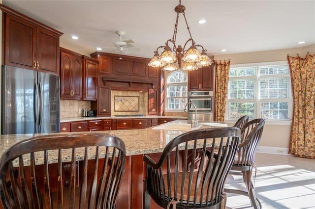 kitchen with appliances with stainless steel finishes, tasteful backsplash, light stone counters, ceiling fan with notable chandelier, and decorative light fixtures