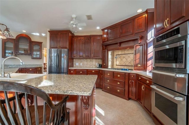 kitchen with backsplash, light stone counters, stainless steel appliances, ceiling fan, and sink