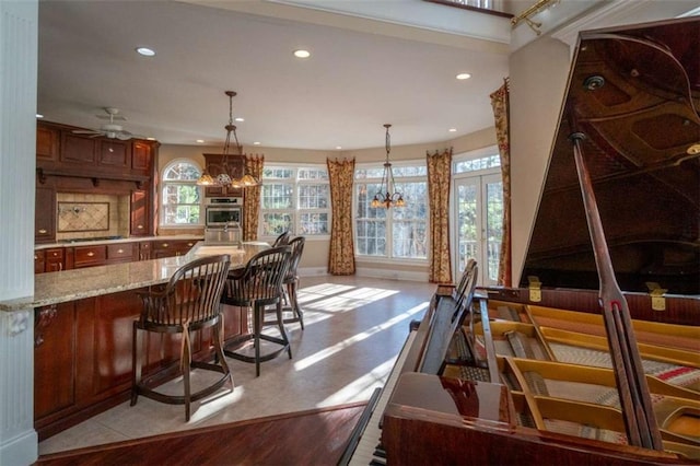 bar featuring ceiling fan with notable chandelier, decorative backsplash, light stone countertops, and hanging light fixtures