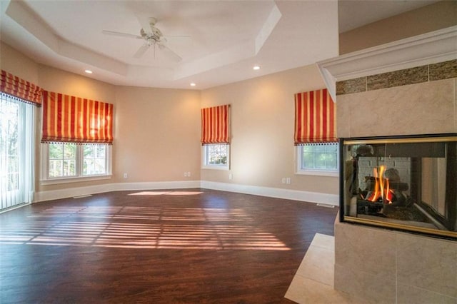 unfurnished living room featuring a multi sided fireplace, dark hardwood / wood-style flooring, a raised ceiling, and ceiling fan