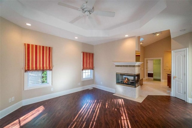 unfurnished living room featuring a tray ceiling, ceiling fan, a multi sided fireplace, and hardwood / wood-style flooring