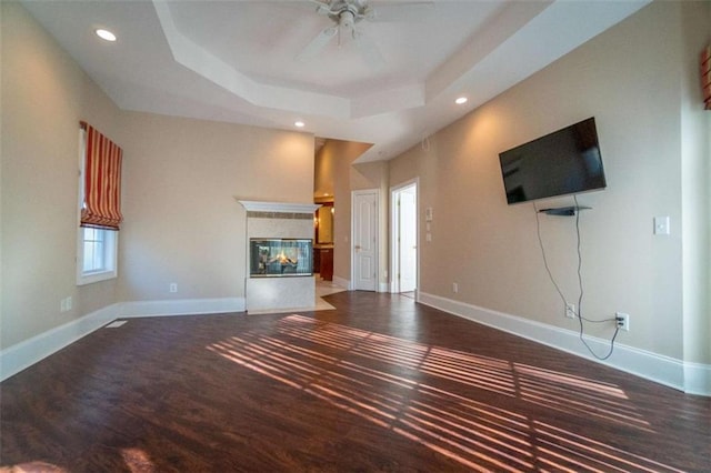 unfurnished living room with a multi sided fireplace, hardwood / wood-style flooring, a raised ceiling, and ceiling fan