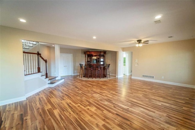 unfurnished living room featuring bar area, light hardwood / wood-style flooring, and ceiling fan