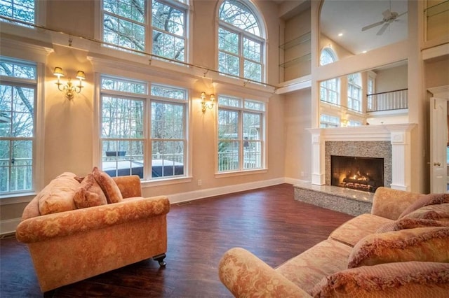 living room with ceiling fan, a fireplace, dark wood-type flooring, and a high ceiling