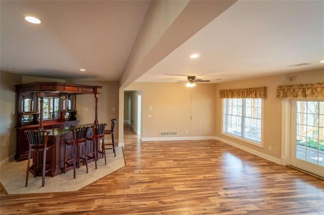 dining space featuring bar, light wood-type flooring, and ceiling fan