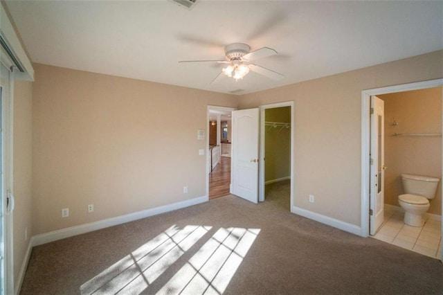 unfurnished bedroom featuring a walk in closet, ensuite bath, light colored carpet, ceiling fan, and a closet