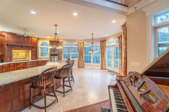 kitchen with light stone countertops, a kitchen breakfast bar, cooktop, ceiling fan with notable chandelier, and pendant lighting