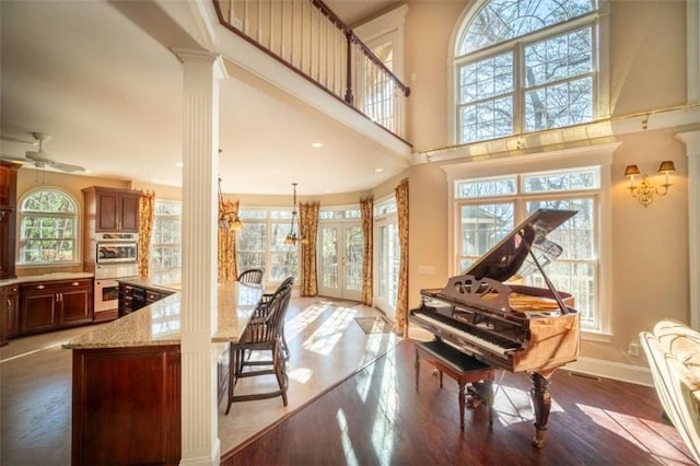 miscellaneous room featuring hardwood / wood-style floors, french doors, ceiling fan, a towering ceiling, and decorative columns