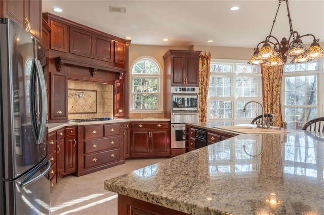 kitchen with sink, stainless steel appliances, light stone counters, backsplash, and decorative light fixtures