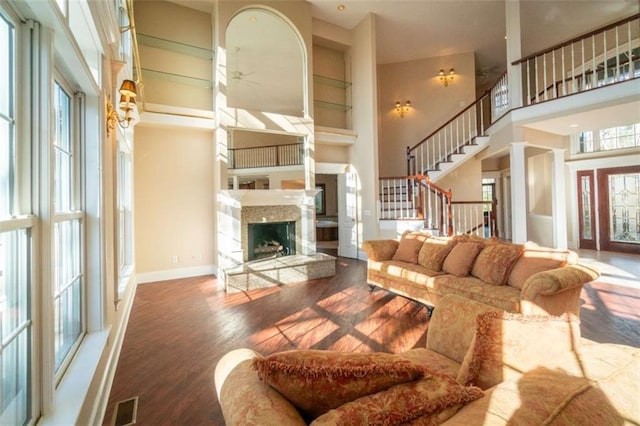 living room with ceiling fan, wood-type flooring, a fireplace, and a high ceiling