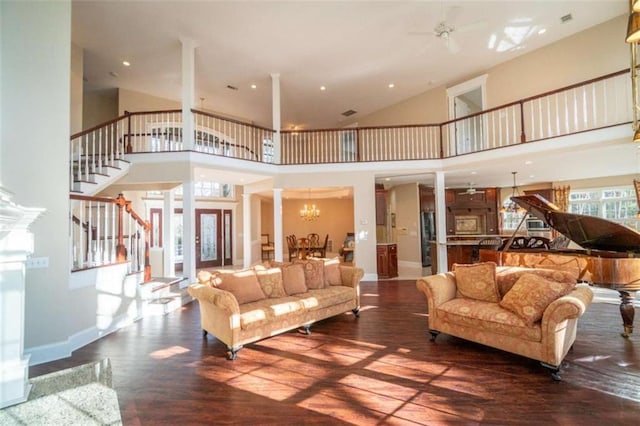 living room with ceiling fan with notable chandelier, dark hardwood / wood-style flooring, a towering ceiling, and ornate columns