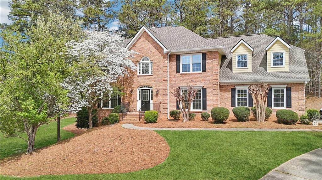 colonial inspired home with brick siding, a shingled roof, and a front lawn
