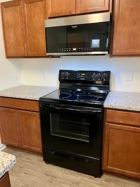 kitchen with light stone counters, light hardwood / wood-style flooring, and black / electric stove