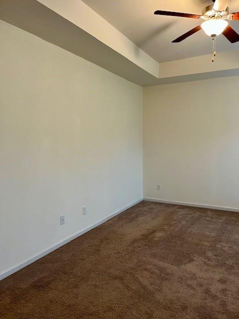 empty room featuring ceiling fan, dark carpet, and a raised ceiling