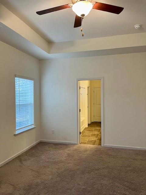 carpeted spare room featuring a raised ceiling and ceiling fan