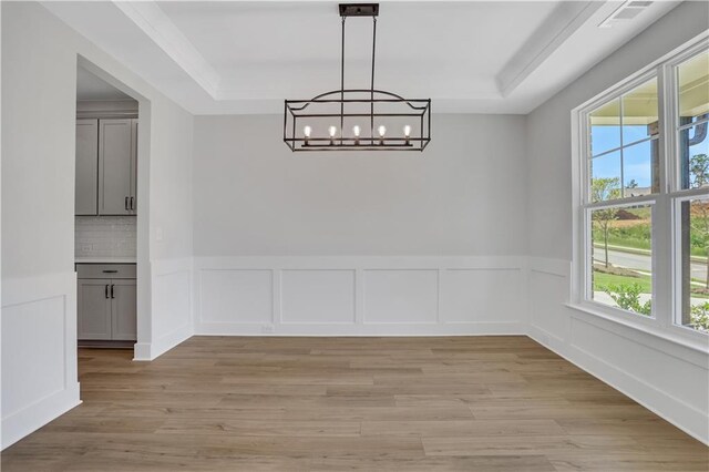 unfurnished dining area featuring a raised ceiling, light hardwood / wood-style flooring, and a notable chandelier