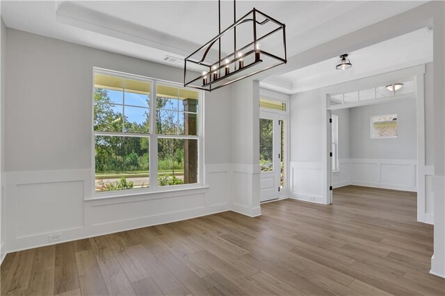 unfurnished dining area with a tray ceiling, an inviting chandelier, and light hardwood / wood-style flooring